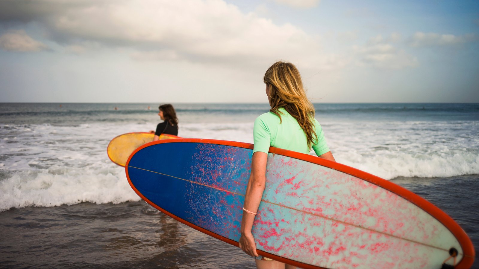 Surfers carrying colorful surfboards into the ocean at a tropical beach.