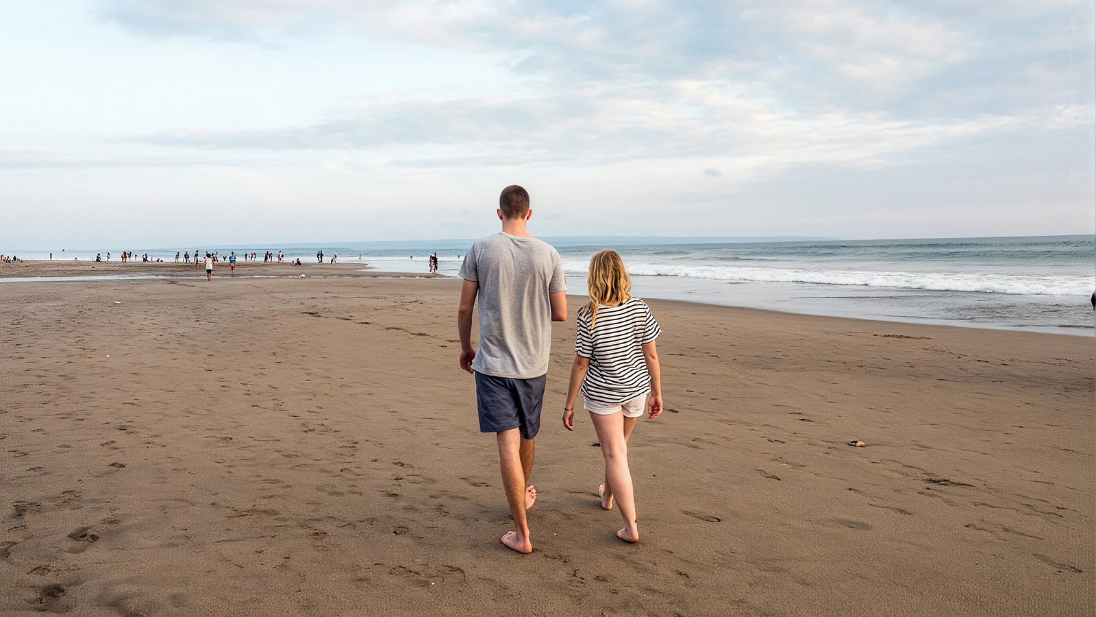 Couple walking barefoot along a wide sandy beach toward the ocean